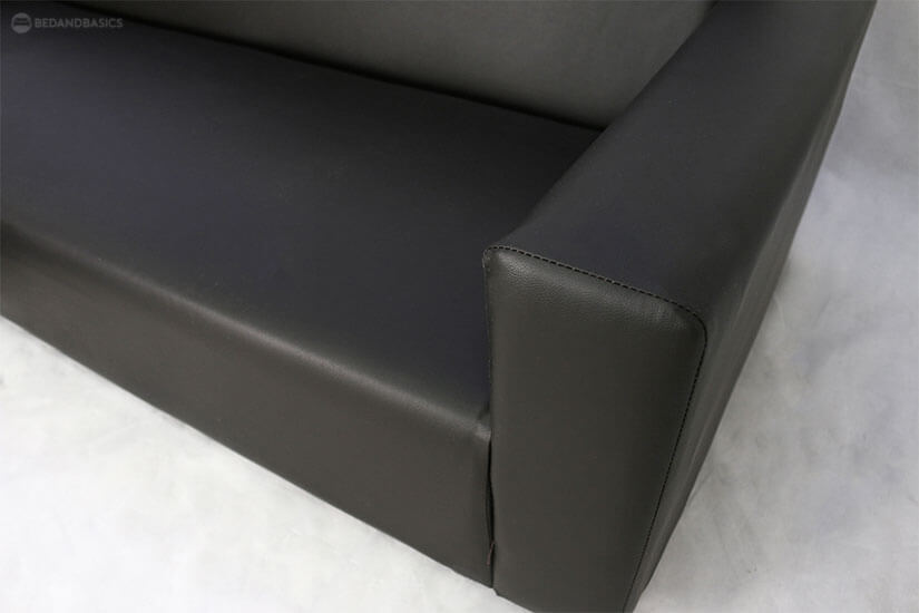The Tess L-Shaped Sofa has a black cloth cover underneath its base, and it is supported by black plastic legs.